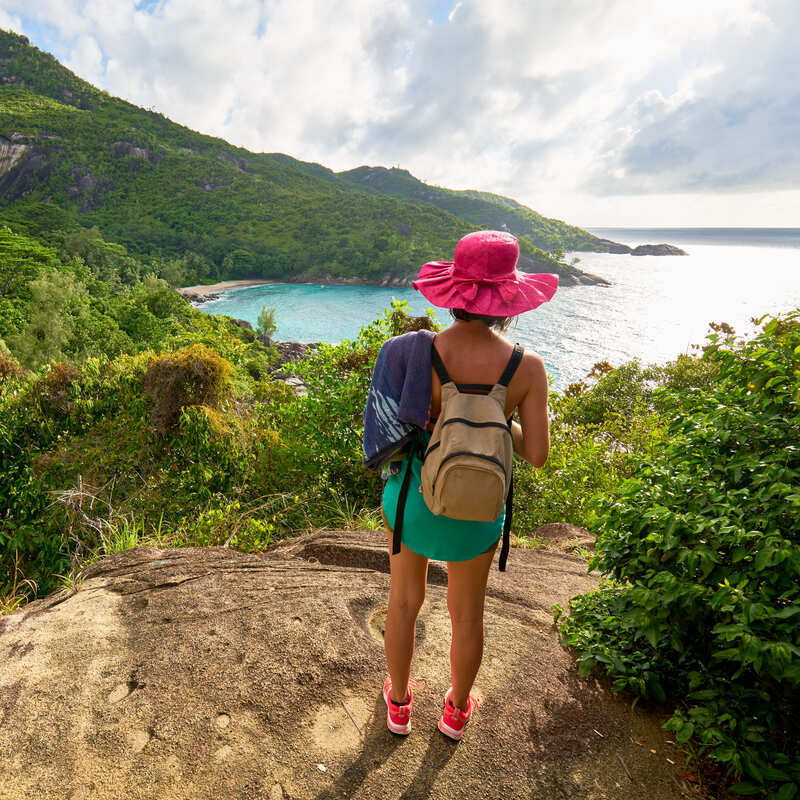 Young Female Tourist Hiking Up The Anse Major Trail In Seychelles, Africa