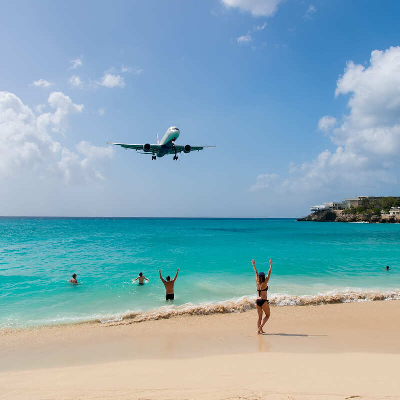 Plane Flying Over Beachgoers In A Tropical Destination, Concept Image For Caribbean Stories