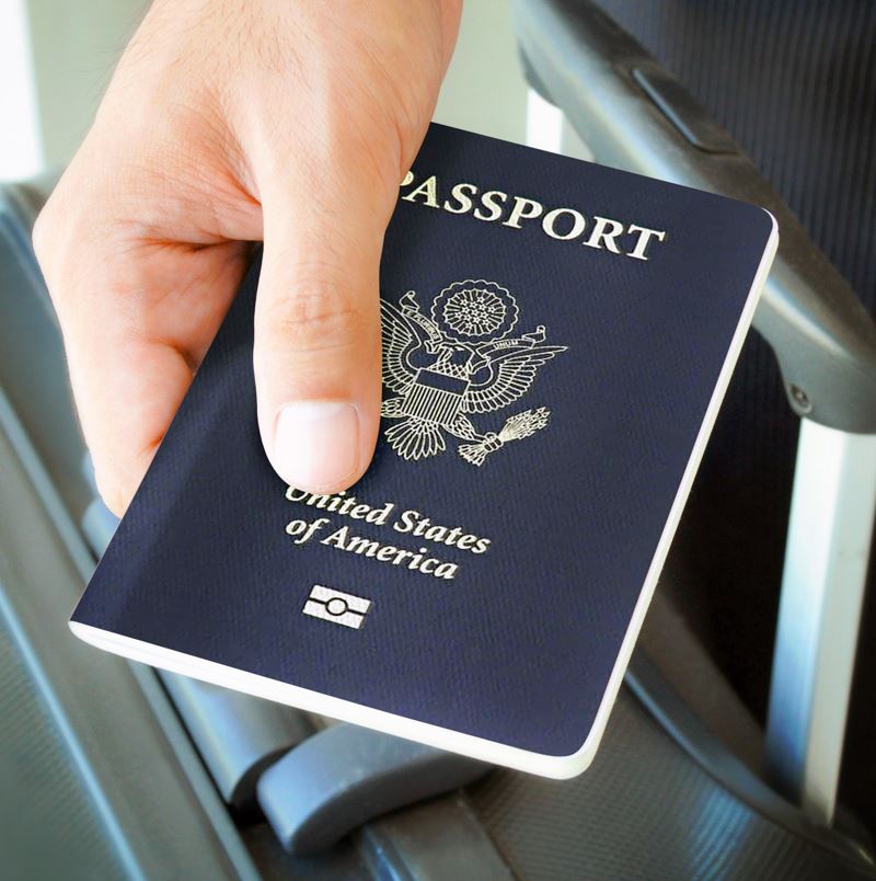 Man holding a passport with a suitcase in the background