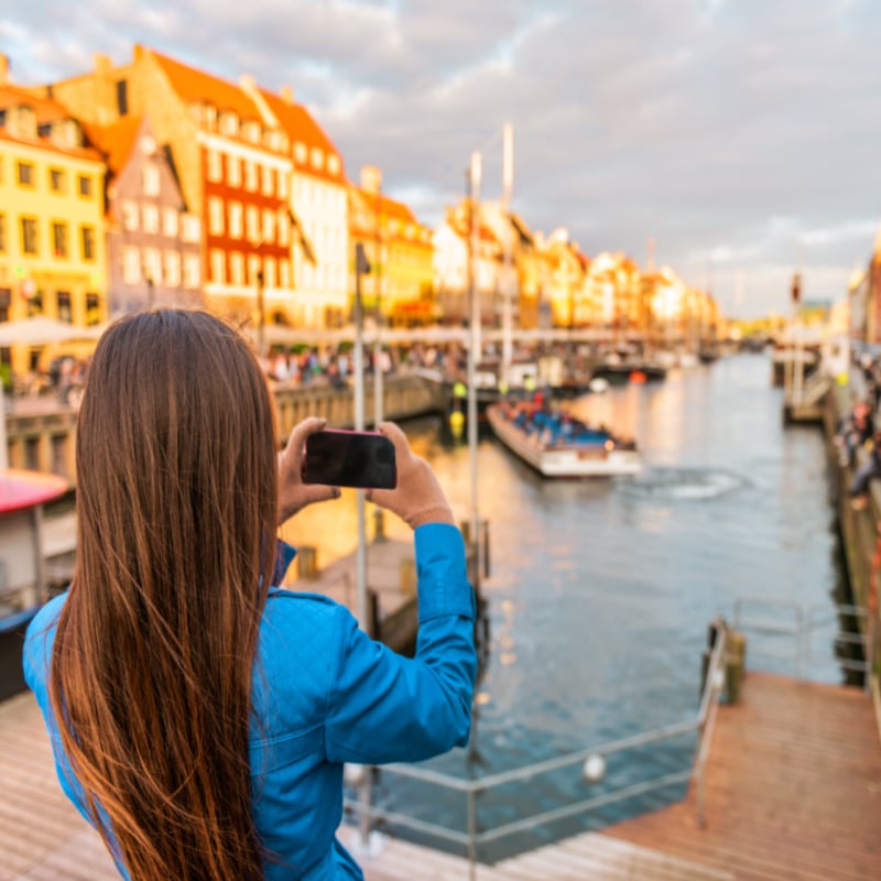 Copenhagen Denmark travel tourist woman taking photo of Nyhavn water canal old town famous tourism destination, attraction in scandinavia, Europe.