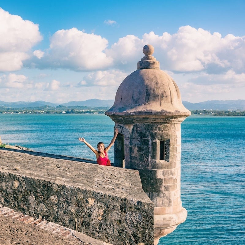 San Juan Puerto Rico travel happy Asian tourist woman excited with open arms in happiness at watch tower of Castillo San Felipe del Morro summer cruise vacation.
